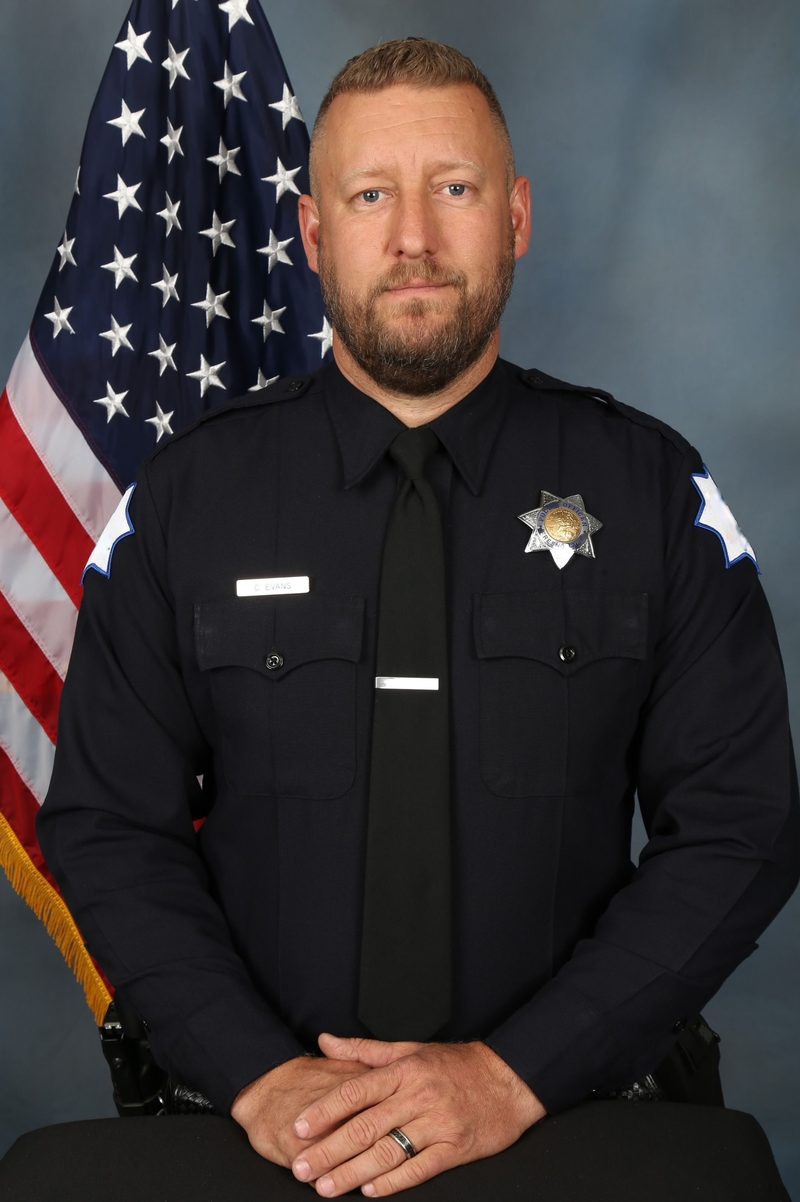 Corey Evans in his formal police department portrait, in uniform in front of the United States flag